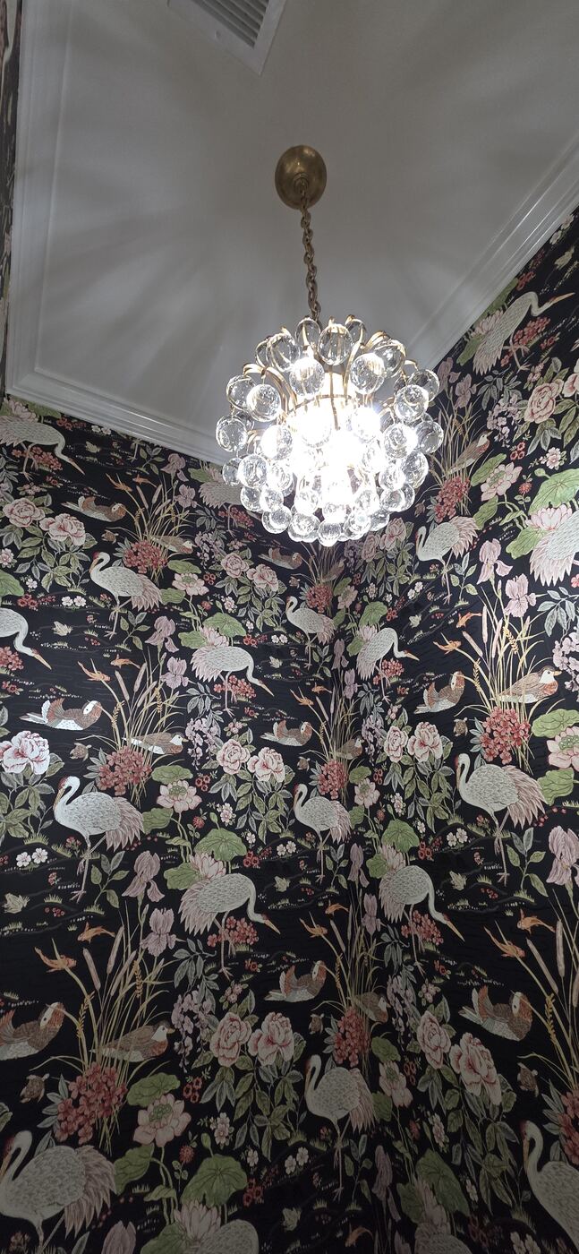 Crystal chandelier installed against a finished decorative powder-room wall.