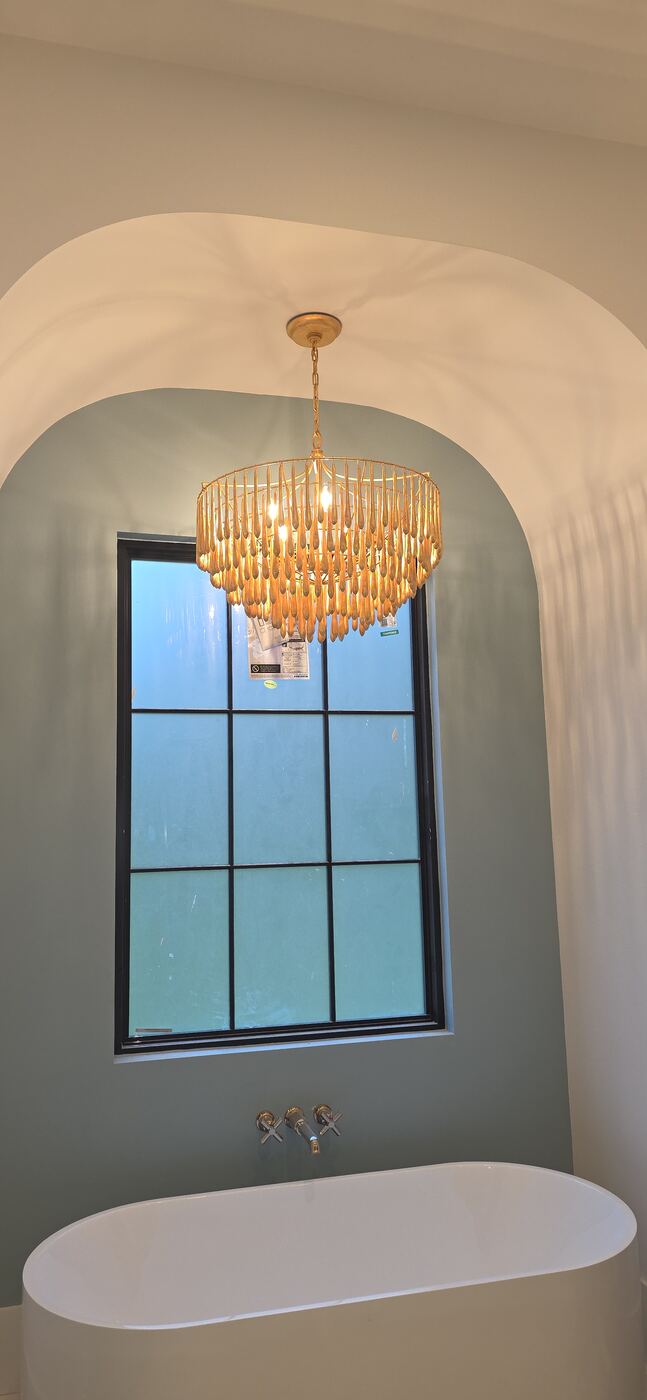 Decorative chandelier installed above a freestanding tub beneath an arched ceiling.